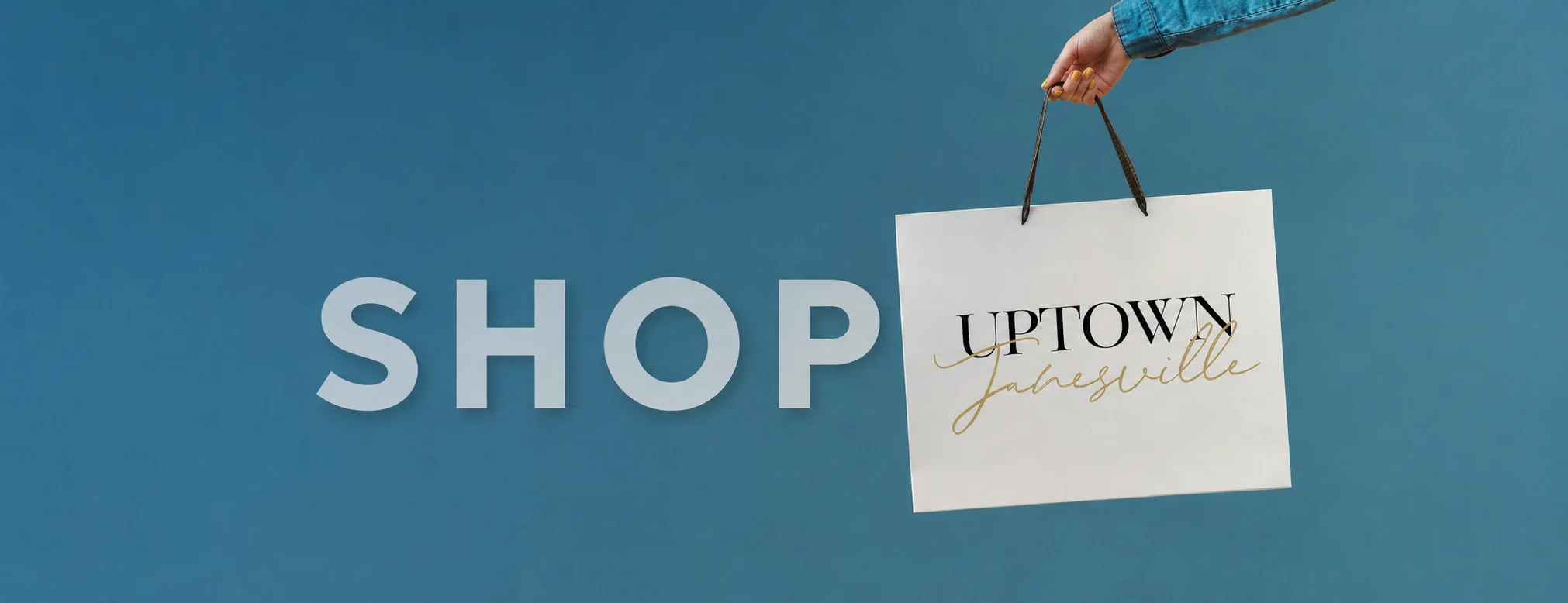 Shop Uptown Janesville: a hand holding an Uptown Janesville shopping bag